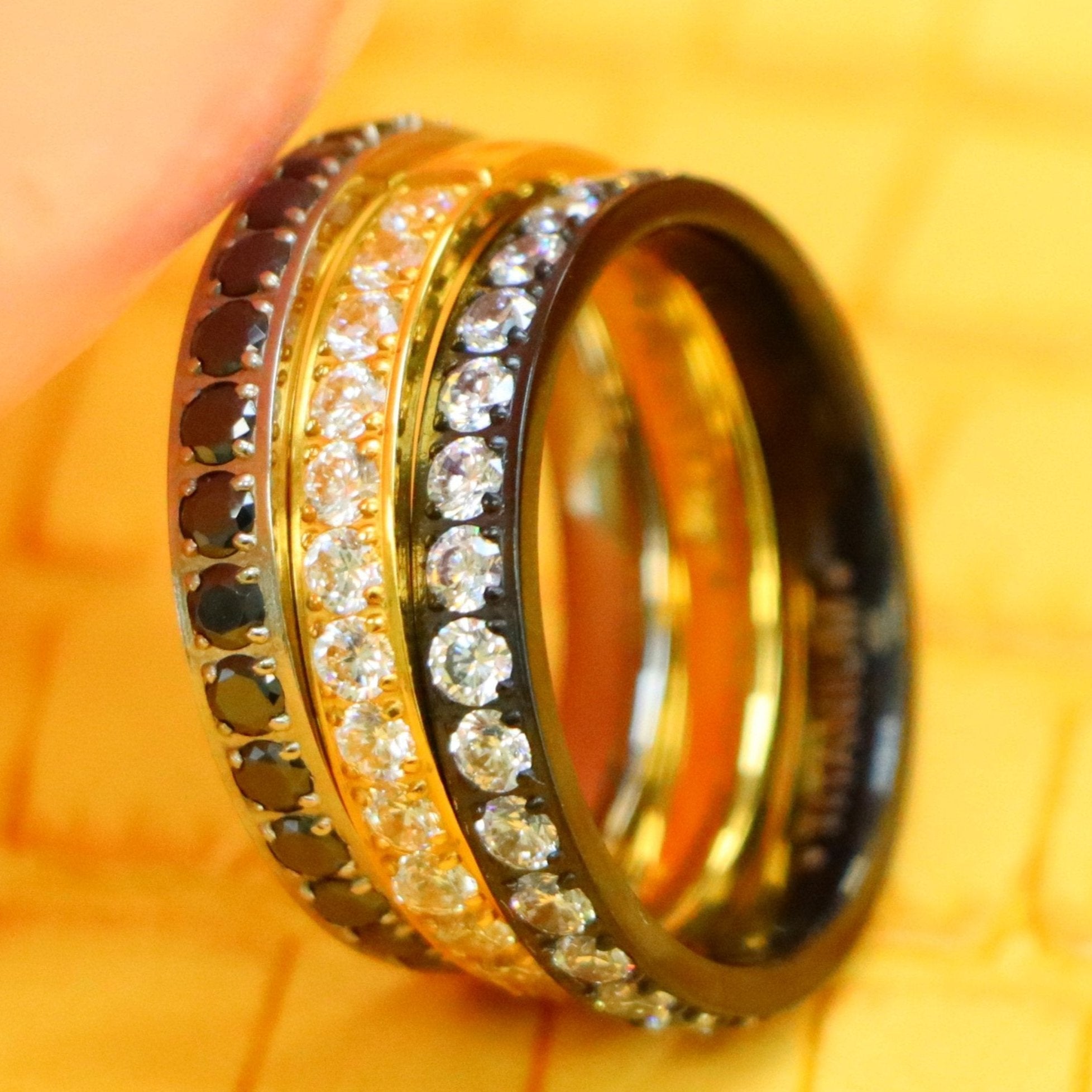Men's and women's 3mm Yellow Gold, Black Plated Full Eternity White CZ Band and 3mm titanium ring Full Eternity black CZ Band supported with a finger from left side