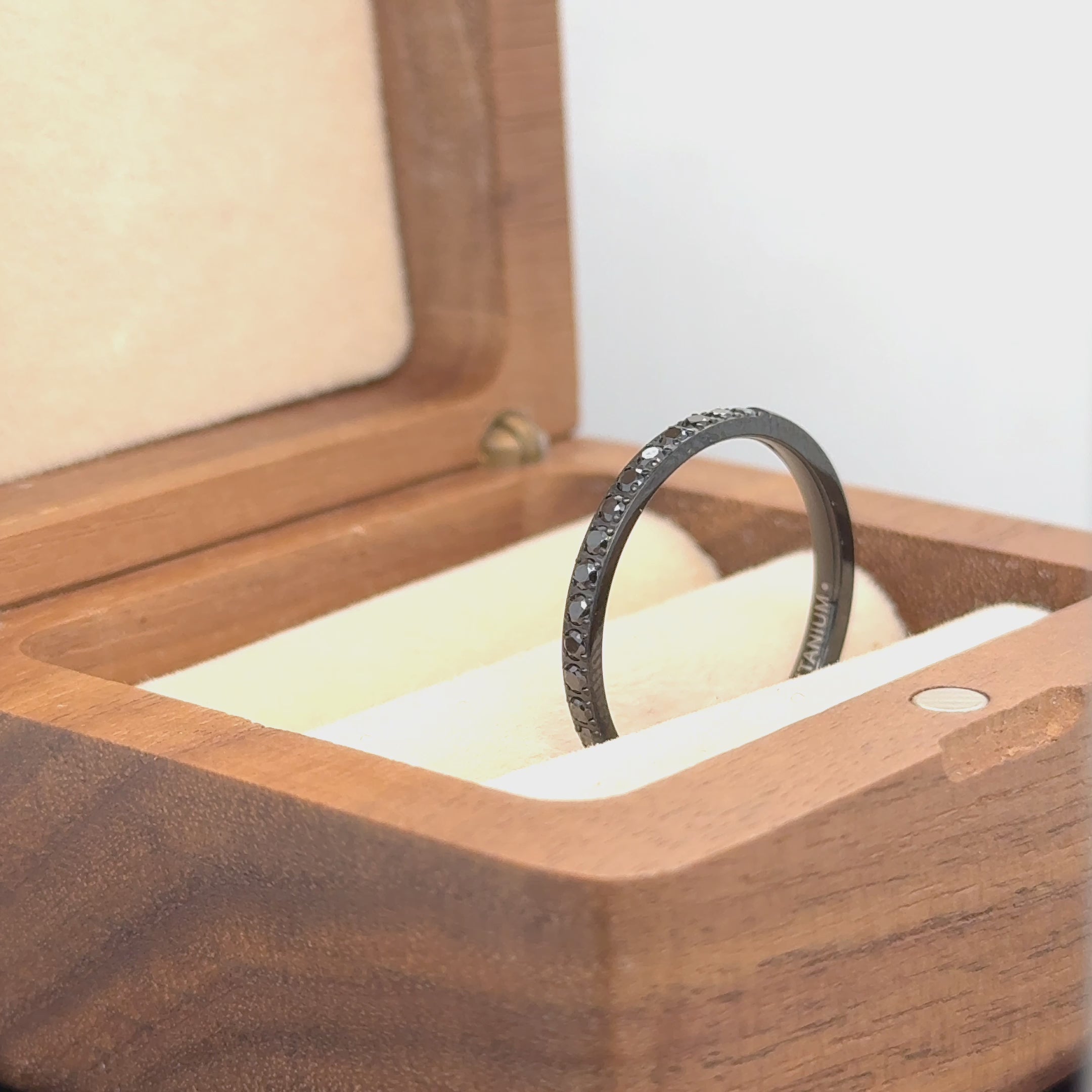 video of 2mm Black Titanium Half Eternity Titanium Ring with black CZ Stones on black titanium ring kept inside a brown box rotating 90 degrees from right to left